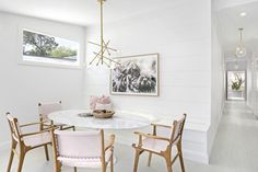 a white dining room with pink chairs and a chandelier hanging from the ceiling