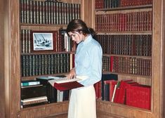 a woman standing in front of a bookshelf holding a book and looking at it