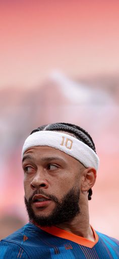 a man with a headband on standing in front of a blurry background and looking off to the side