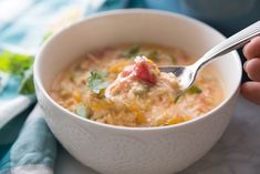 a hand holding a spoon full of soup with cheese and vegetables in it, on top of a white bowl