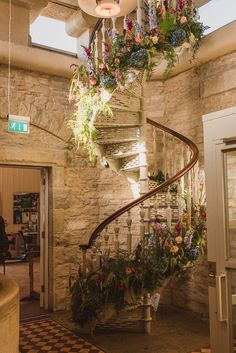 a spiral staircase with flowers hanging from it's sides in a stone walled building