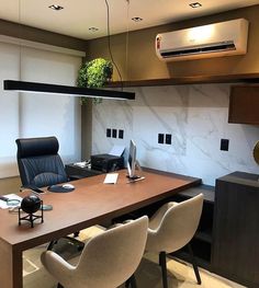 an office desk with two chairs and a computer monitor on it, in front of a wall mounted air conditioner