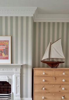 a toy sailboat on top of a dresser in a room with striped wallpaper