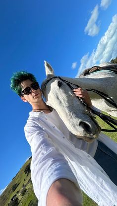 a man with green hair standing next to a white horse