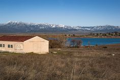 an old building sits in the middle of a field with snow capped mountains behind it