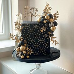 a black and gold birthday cake sitting on top of a table next to a window