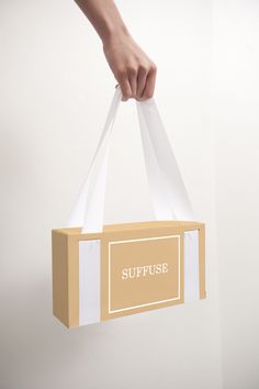 a person holding a paper bag with the word suffuse printed on it in gold and white