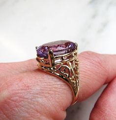 "This is a vintage 10K yellow gold filled filigree ladies ring. It is set with a large oval amethyst gemstone. The stone measures 11.9mm x 15.9mm. There is a natural inclusion in the amethyst that you will see throughout the pictures. The band is sized at a 7. Total weight of the ring is 5.3grams/3.4dwt. The band is stamped 10K inside. There is a hallmark that is an \"F\" inside a diamond shape. This is a vintage, previously owned ring. Therefore, light wear can be expected. There is no visible Ladies Ring, Amethyst Gem, Purple Band, Gold Filigree, Tennis Bracelet Diamond, Wrap Rings, Diamond Shape, Amethyst Gemstone, Silver Leaf