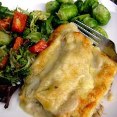 a white plate topped with lasagna covered in cheese next to salad and a fork