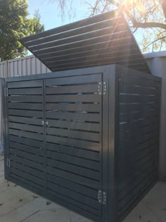 a large metal box sitting on top of a sidewalk next to a tree and fence