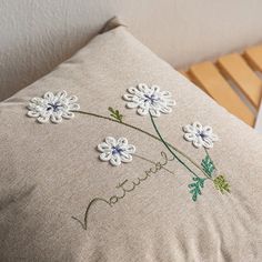 a pillow with embroidered flowers on it sitting next to a wooden bed headboard and chair