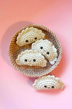 three small crocheted bears in a basket on a pink surface with one laying down and the other lying down