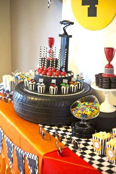 a table topped with lots of cupcakes and cake next to a black tire