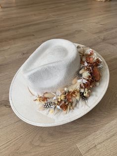 Introducing this handcrafted fedora with an intricate floral embroidery, a unique and stylish handmade hat that will elevate your fashion game to the next level. Made with high-quality materials and great attention to detail, this wide brim fedora hat is designed to provide you with comfort, style, and durability.   Highlights:  - Handmade with great attention to detail  - Features a multicolor dried floral crown tied band - Comes in a classic white color that can easily pair             with an Elegant Cream Luxury Fedora, Bohemian Fedora With Short Brim For Party, Handmade White Fedora For Spring, Bohemian Fedora Costume Hat For Summer, Bohemian Short Brim Fedora For Party, White Wide Brim Festival Hat, White Wide Brim Costume Hat For Festival, White Bohemian Fitted Hat, Handmade Adjustable White Felt Hat