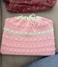 a crocheted pink hat sitting on top of a couch next to a purse