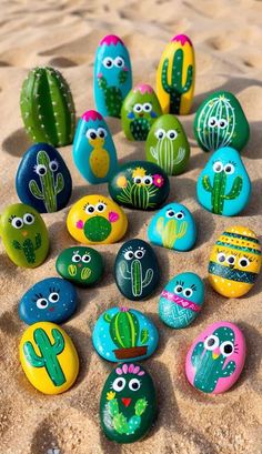 rocks painted with different colors and designs on the sand, including cacti and succulents