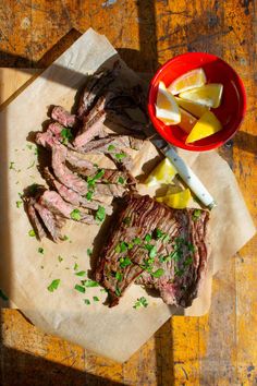 sliced meat and vegetables on a cutting board with a bowl of lemons next to it