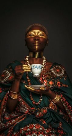 an african woman holding a cup and saucer in her hands with gold paint on her face