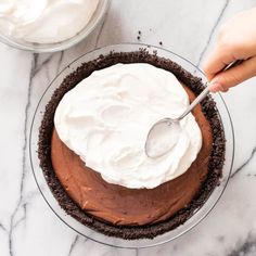 someone is spreading icing on the top of a chocolate pie with white frosting