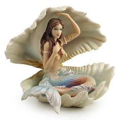 a mermaid figurine sitting on top of a shell with her hands behind her head