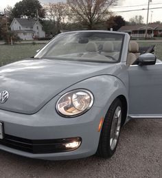 the front end of a gray convertible car parked in a parking lot next to a house