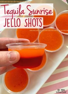 a person holding up a small cup filled with jello shots on top of a white plate