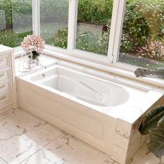 a white bath tub sitting next to a window in a room with marble flooring