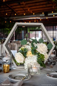 a centerpiece with white flowers and greenery on a table