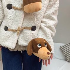 a person holding a stuffed animal dog in their hand and wearing a white jacket with brown trim