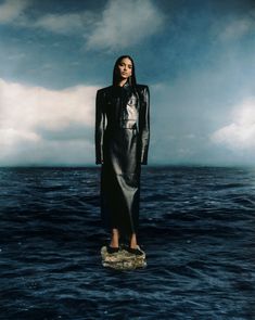 a woman standing on top of a rock in the middle of an ocean with clouds