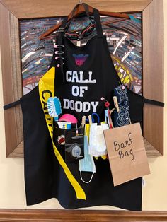 a black apron hanging on a wall next to a sign that says, call of doody