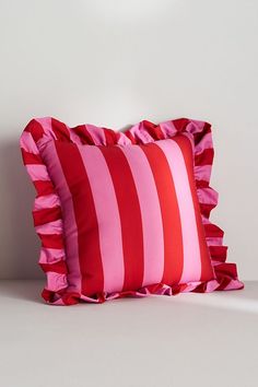 two red and pink pillows sitting next to each other on a white surface with a light in the background