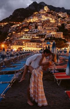 a man and woman kissing on the beach at night with umbrellas in the foreground