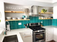 a kitchen with white cabinets and blue tile backsplash, stainless steel range hood