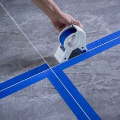 a person using a tape measure to measure the width of a tile floor with blue tape