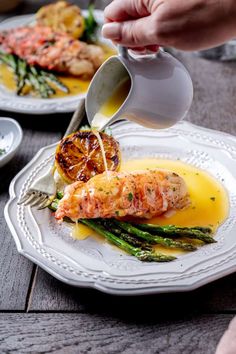 a person pouring sauce on top of asparagus and shrimp in a white plate