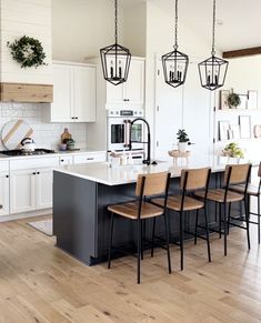 a large kitchen with white cabinets and black island in the center, surrounded by wooden flooring