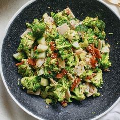 a black plate filled with broccoli and other vegetables on top of a table