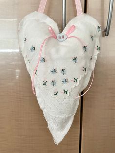 a heart shaped pillow hanging from a hook on a wooden door with pink ribbon and white lace