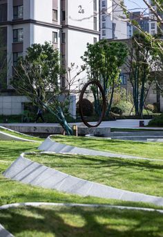 an artistic sculpture in the middle of a grassy area with trees and buildings in the background