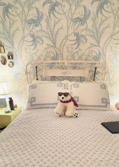 a white dog sitting on top of a bed next to a pillow and lamp in a bedroom