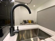 a kitchen sink sitting under a faucet next to a counter top with a couch in the background