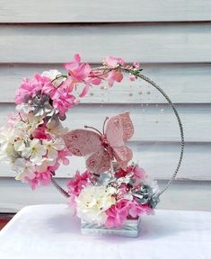 a pink and white flower arrangement in a metal ring with butterflies on it's sides