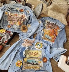 two jean jackets with patches on them sitting on top of a wooden table next to other items