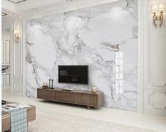 a living room with white marble walls and flooring, along with a flat screen tv mounted on the wall