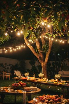 an outdoor dinner is set up under a tree with lights strung from the branches over it