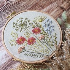 a close up of a embroidery on a wooden surface with dried grass and flowers in the background