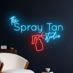 the spray tan studio neon sign is lit up in front of a chair and coffee table