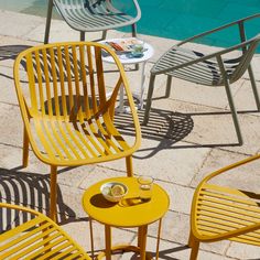 yellow chairs and tables next to a swimming pool