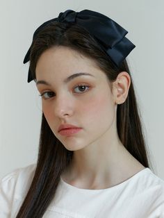 a woman with long hair wearing a white shirt and a black bow on her head